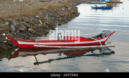 Banay Banay Banay, Davao Oriental, Philippines - Mars 2016 : petit bateau à outrigger rouge et blanc amarré près de la rive d'un lagon. Banque D'Images