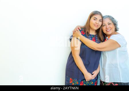 Mère embrassant sa fille avec beaucoup d'amour, deux femmes mexicaines souriantes sur un fond blanc, espace pour le texte Banque D'Images