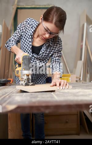 Charpentier brunette travaillant avec la scie à métaux en atelier. Banque D'Images