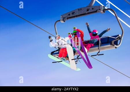 Équipe amusante d'amis skieur et snowboarders jusqu'à la remontée mécanique sur fond bleu ciel Banque D'Images