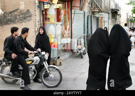 Filles et garçons, discuter dans la rue. La fille porte un chador, les garçons s'assoient sur une moto, Yazd, Iran. Banque D'Images