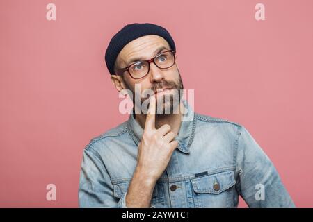 L'homme barbu réfléchi profondément dans pensées, regarde avec pensive expression en huis clos, concentré sur quelque chose, pose contre fond rose. P Banque D'Images