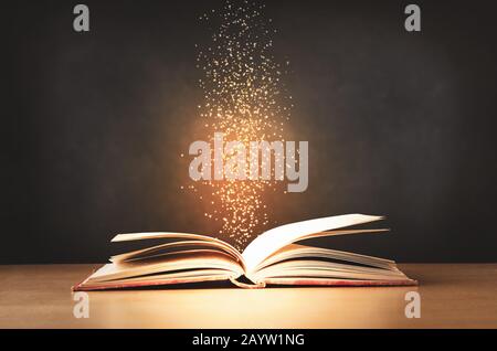 Un vieux livre de texte rouge, porté, couché ouvert sur un bureau de classe avec des étincelles et des étoiles s'élevant vers le haut de son centre. Fond noir du tableau de surveillance. Banque D'Images