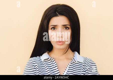 Brunette sombre jeune femelle couts lèvres en discontent, étant insatisfait de quelque chose, a une peau pure saine, yeux sombres et maquillage, vêtu de cas Banque D'Images