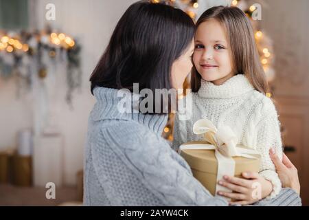 Jeune femme embrasse son petit enfant, donne à présent, félicite avec Nouvelle année, fier d'avoir une si belle et intelligente fille. Happy kid passe Banque D'Images