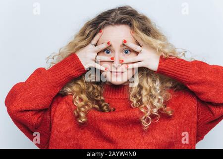 Portrait horizontal d'une mystérieuse femelle aux yeux bleus avec des cheveux caillés, couvre le visage avec les mains, vêtu d'un pull rouge ample, isolé sur la ba blanche Banque D'Images