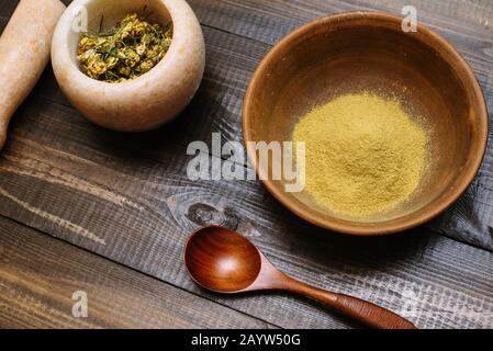 Mortier de marbre avec camomille séchée pour cosmétiques naturels. Bol en argile avec poudre jaune ou argile et fleurs sur fond en bois. Pose plate. Banque D'Images