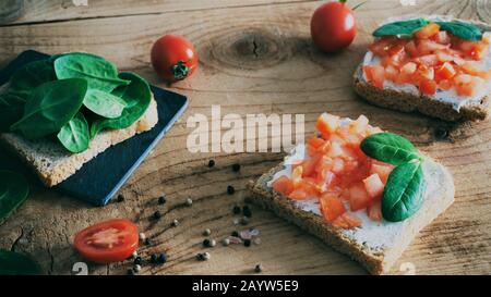 Plat de sandwichs végétaliens avec des tomates tranchées au fromage à la crème et des jeunes épinards petit déjeuner sain manger un régime végétarien Banque D'Images