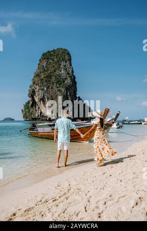 Railay Beach Krabi Thaïlande, couple marchant le matin sur la plage avec des falaises tropicales et de longs bateaux à queue sur l'arrière-plan à l'île de Banque D'Images