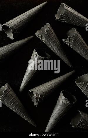 Cornets ou cônes de glace de gaufre gris monochromatiques créatifs dispersés sur le noir dans une texture de fond plein cadre d'en haut Banque D'Images