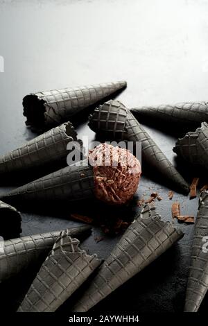 Diffusion aléatoire de cônes de glace gris avec une pelle au chocolat recouverte de flocons dans le cornet central sur un fond gris dégradé avec espace de copie Banque D'Images