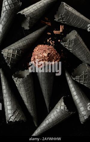 Fond de cône de glace monochromatique gris foncé avec une seule pelle de glace au chocolat brun recouverte de flocons dans le cornet central Banque D'Images