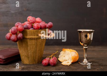 Tasse avec vin, pain, raisins et bible sur table bizarre Banque D'Images