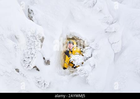 femme souriante se posant dans une petite grotte naturelle dans un rocher enneigé Banque D'Images
