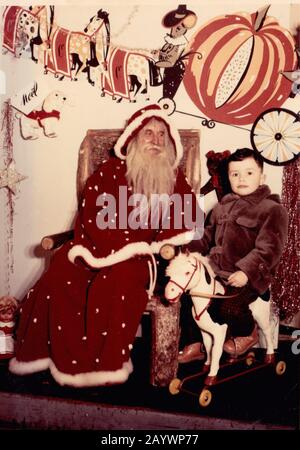 Photographie d'un petit garçon sur un cheval à bascule à côté de Santa Claus Banque D'Images