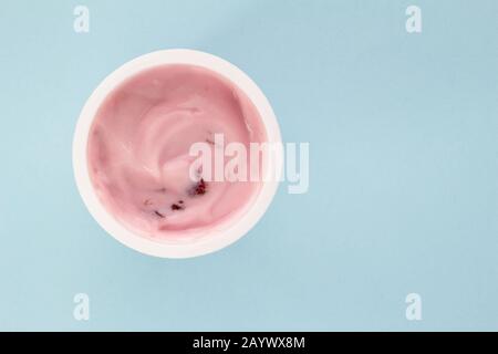 Yaourt dans une tasse en plastique vue de dessus. Photo de yaourt à la fraise isolée sur fond bleu pâle avec espace texte Banque D'Images