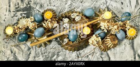 Bannière de Pâques : composition à partir d'œufs bleus, formes de gâteau, branches d'arbres, fleurs sèches et bougies sur fond de béton, espace de copie, religieux chrétien Banque D'Images