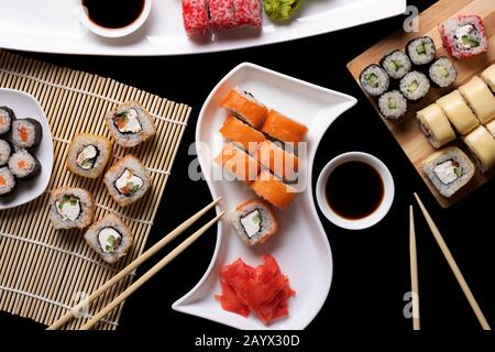 Ensemble de plats traditionnels japonais sur un fond sombre. Petits pains à sushi, nigiri, steak de saumon cru, riz, fromage à la crème, avocat, citron vert, gingembre mariné. Banque D'Images