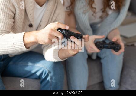 Gros plan d'amis non reconnaissables dans des vêtements décontractés à l'aide de joysticks tout en s'amusant avec le jeu vidéo Banque D'Images