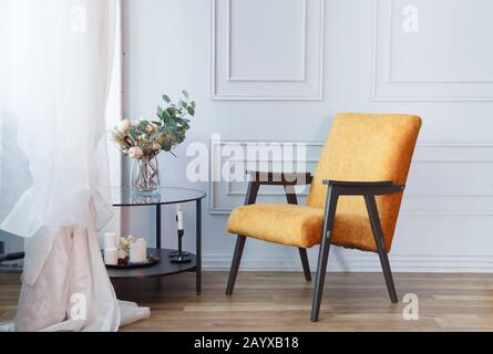 Intérieur d'un salon contemporain avec fauteuil orange, table en verre et cadre en plâtre au mur Banque D'Images