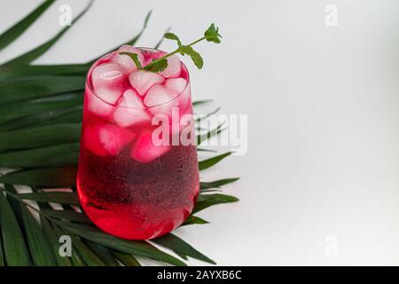 Boisson aux framboises et aux baies dans un verre transparent avec de la glace. Ajout de branches de palmiers et de framboises. Fond blanc. Espace de copie Banque D'Images