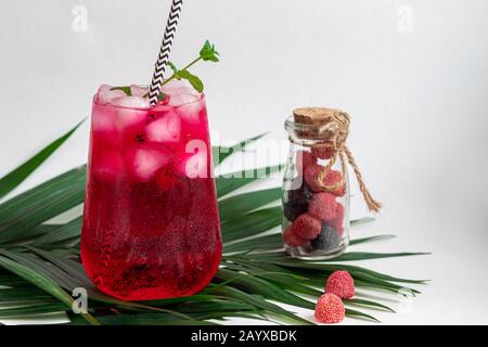 Boisson aux framboises et aux baies dans un verre transparent avec de la glace. Ajout de branches de palmiers et de framboises. Fond blanc. Espace de copie Banque D'Images