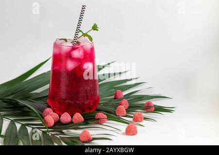 Boisson aux framboises et aux baies dans un verre transparent avec de la glace. Ajout de branches de palmiers et de framboises. Fond blanc. Espace de copie Banque D'Images