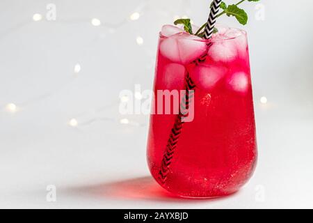 Boisson aux framboises et aux baies dans un verre transparent avec de la glace. Ajout de branches de palmiers et de framboises. Fond blanc. Espace de copie Banque D'Images