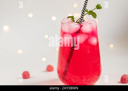 Boisson aux framboises et aux baies dans un verre transparent avec de la glace. Ajout de branches de palmiers et de framboises. Fond blanc. Espace de copie Banque D'Images