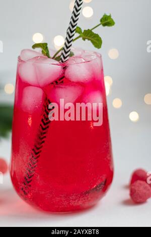 Boisson aux framboises et aux baies dans un verre transparent avec de la glace. Ajout de branches de palmiers et de framboises. Fond blanc. Espace de copie Banque D'Images