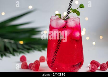 Boisson aux framboises et aux baies dans un verre transparent avec de la glace. Ajout de branches de palmiers et de framboises. Fond blanc. Espace de copie Banque D'Images