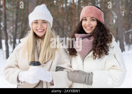 Photo horizontale moyenne de deux jeunes femmes portant des vêtements élégants et chauds debout ensemble à l'extérieur le jour d'hiver regardant l'appareil photo souriant Banque D'Images