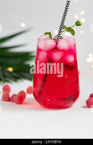 Boisson aux framboises et aux baies dans un verre transparent avec de la glace. Ajout de branches de palmiers et de framboises. Fond blanc. Espace de copie Banque D'Images