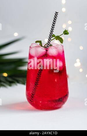 Boisson aux framboises et aux baies dans un verre transparent avec de la glace. Ajout de branches de palmiers et de framboises. Fond blanc. Espace de copie Banque D'Images