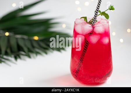 Boisson aux framboises et aux baies dans un verre transparent avec de la glace. Ajout de branches de palmiers et de framboises. Fond blanc. Espace de copie Banque D'Images