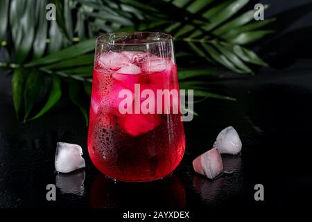 Boisson aux framboises et aux baies dans un verre transparent avec de la glace. La boisson est versée dans un verre. Ajout de branches de palmiers et de framboises. Fond noir. Cop Banque D'Images