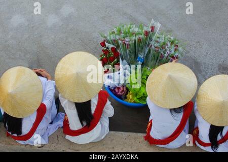 Les femmes portant des robes traditionnelles (Ao Dai) et des chapeaux de cône (non la) assis dans le port de qui Nhon dans le centre du Vietnam attendant d'accueillir les touristes de Banque D'Images