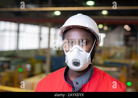 Tête horizontale et épaules portrait d'un homme noir non reconnaissable en usine avec masque de protection regardant l'appareil photo Banque D'Images