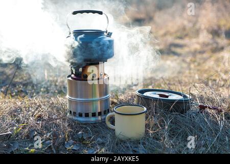 préparation du thé en plein air. eau bouillante dans la bouilloire sur le brûleur portable en bois avec fumée Banque D'Images