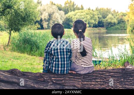 Deux enfants, un garçon et une fille, assis ensemble sur un tronc d'un arbre et regarder au paysage de lac Banque D'Images