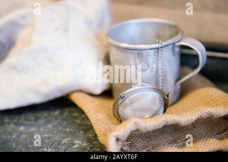 Théière en métal avec oeuf à thé derrière la serviette blanche en coton. Style rustique vintage Banque D'Images