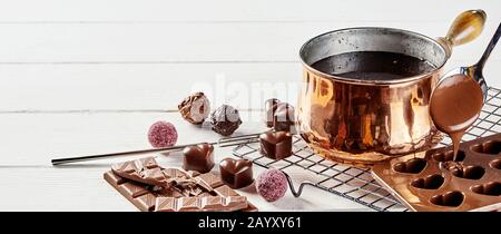 Fabrication de bonbons au chocolat en forme de coeur de Valentines qui versent du chocolat fondu dans des moules à partir d'une casserole en cuivre sur un support de cuisine en fil métallique dans une bannière panoramique Banque D'Images