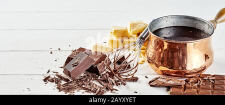 Fouetter une sauce de chocolat fondu dans une poêle en cuivre avec un fouet à la main et des barres assorties de chocolat en coppé sur un fond de bois blanc avec copie Banque D'Images