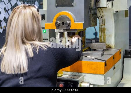 Une femme blonde avec des cheveux longs travaillant avec la presse mécanique d'estampage dans l'usine de travail de métaux sans vêtements de travail de sécurité. Banque D'Images