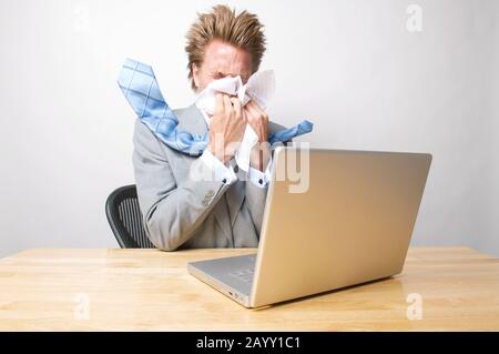 Un travailleur de bureau allergique éternuant devant son ordinateur portable à l'intérieur de son bureau Banque D'Images