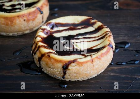 Mini-Cheesecakes avec sauce au chocolat noir: Paire de cheesecakes individuels coulis avec sauce au chocolat noir Banque D'Images