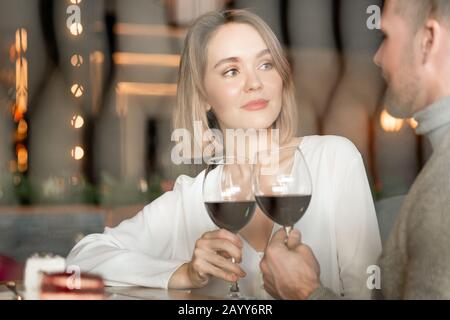 Portrait horizontal d'une jolie femme caucasienne et d'un homme assis dans des verres de clinking au restaurant avec du vin rouge Banque D'Images