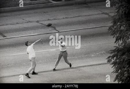 Années 60, historique, vue aérienne de deux jeunes hommes américains dans la rue, peut-être étudiants d'université, jouant au football américain, Californie, États-Unis. Banque D'Images