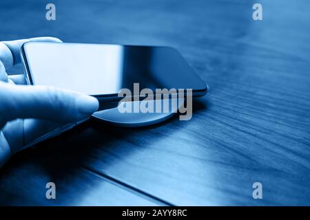 La main tient un smartphone mobile pour le chargement sans fil en partageant la batterie via un appareil dans une couleur bleue classique. Technologie de charge. Partage Des Frais De L'Appareil Technique. Gros plan. Banque D'Images