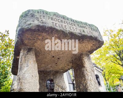 Détail d'un monument funéraire en pierre blanche et tête métallique avec le fond d'arbres et d'autres chapelles funéraires sous un ciel terne Banque D'Images